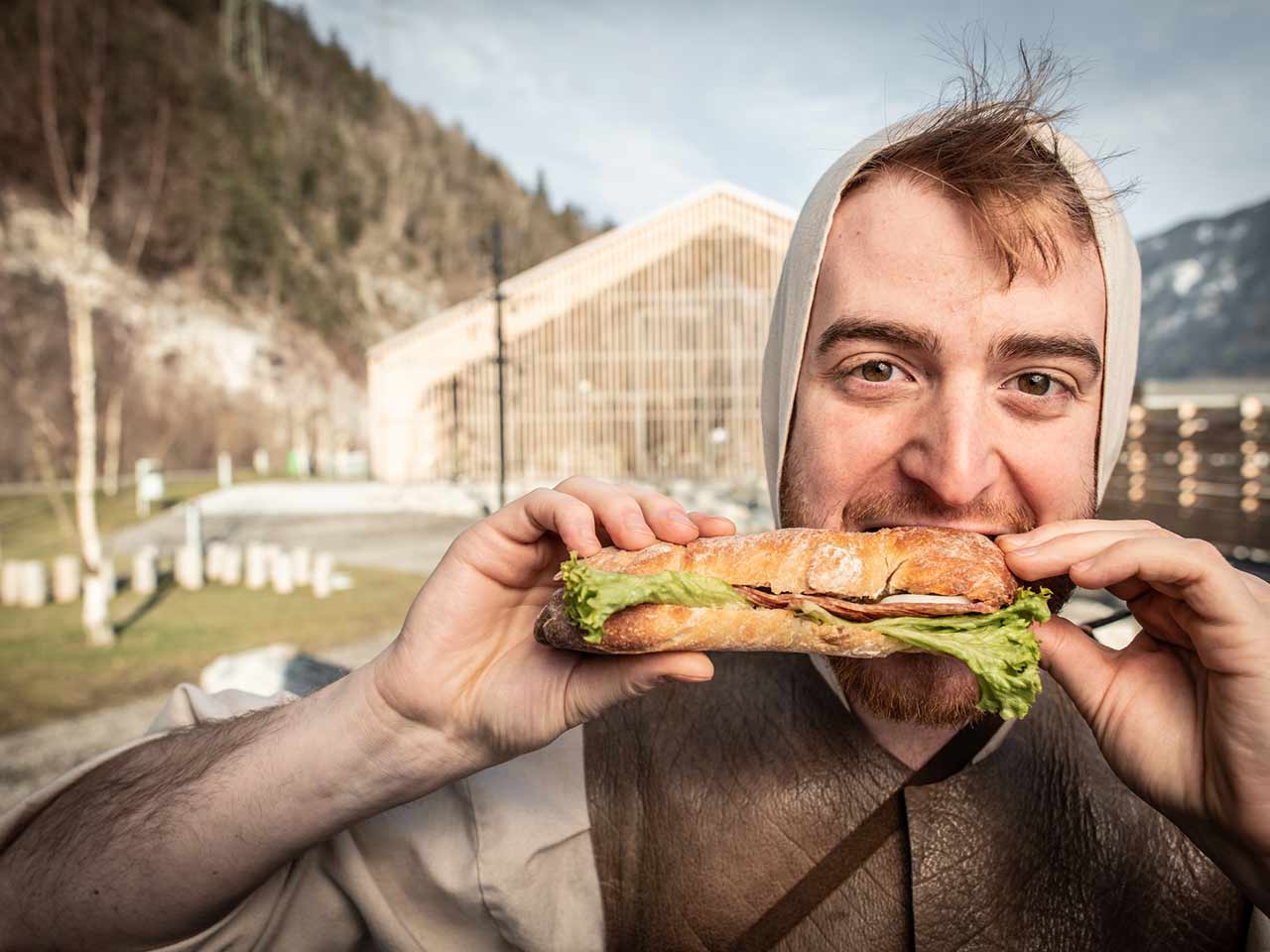 William Tell bites into a salami, salad and egg sandwich