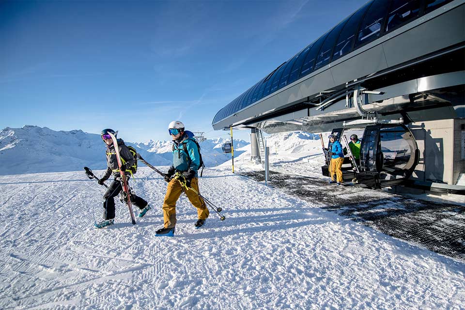 Skifahrer steigen aus einer Gondelbahn inmitten verschneiter Berggipfel 