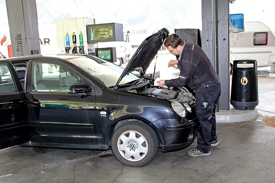 Mann vor geöffneter Motorhaube prüft den Motorölstand