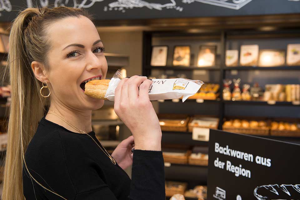 Young woman biting joyfully into a nut croissant